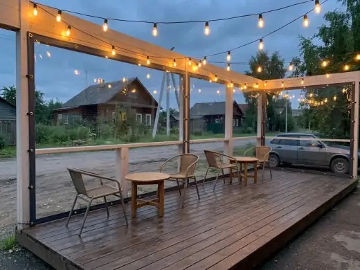 The result: the same terrace in the evening — the bays covered with clear soft windows with dark edging and straps, a warm garland of retro bulbs glowing under the top beam